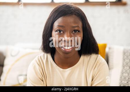 Close up portrait of the pretty multiracial girl sitting at the sofa at home and looking into the camera, looking happy. Indoor Stock Photo