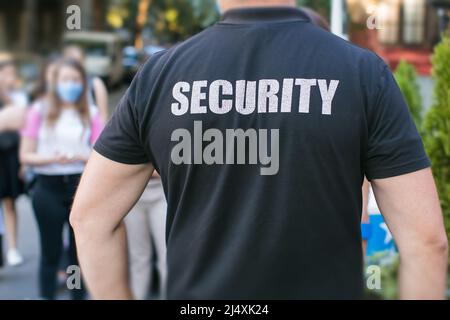 security guard standing on street in front of crowd wearing face masks Stock Photo