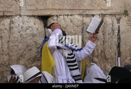A Jewish worshiper wrapped with the Ukrainian flag and Talit prayer shawl prays as religious Jews of the Cohanim Priestly caste take part in the bi-annual mass 'Birkat Kohanim' or 'Priestly Blessing' on the holiday of Pesach (Passover) at the Kotel in Jerusalem, Israel. Stock Photo