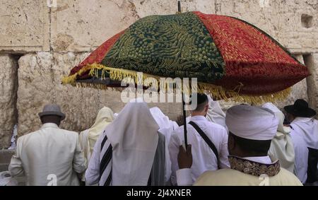 A white turbaned religious priest from the Beta Israel community holds traditional colorful umbrellas as ultra-Orthodox Jews of the Cohanim Priestly caste take part in the bi-annual mass 'Birkat Kohanim' or 'Priestly Blessing' on the holiday of Pesach (Passover) at the Kotel in Jerusalem, Israel. Stock Photo