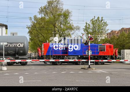 Basel, Switzerland - April 2022: Diesel shunter locomotive pulling a train of oil tankers crossing a road in the city's port on the Rhine River Stock Photo