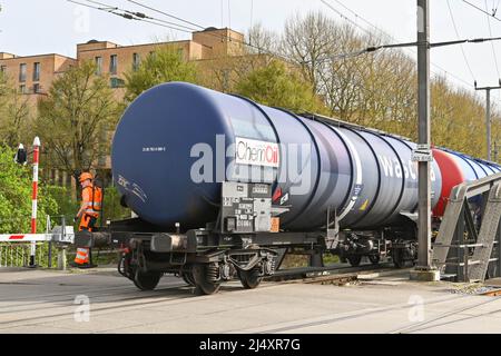 Basel, Switzerland - April 2022: Railway worker riding on the end of a train of oil tankers crossing a road in the city's port on the Rhine River Stock Photo