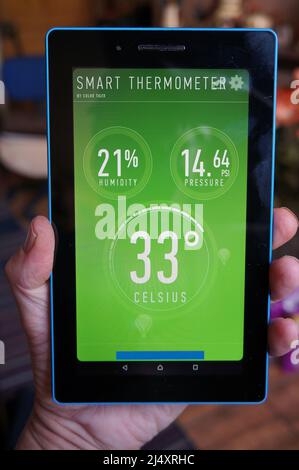 Hand holding a tablet PC showing 33c temperature & humidity on the weather app Stock Photo