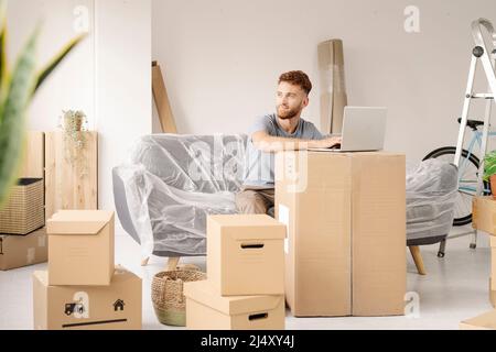 A young man resting from moving into his new home using his laptop. Stock Photo