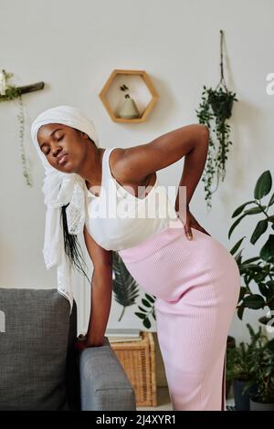 African muslim pregnant girl leaning on sofa suffering from pain in her back during contraction Stock Photo