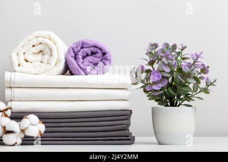 Stack of bed linen, sheets and towels with cotton branch and potted plant on table Stock Photo