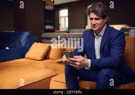 Mature Caucasian man, businessman, entrepreneur, sales rep, retail manager holding a mobile phone, typing text messages, surfing, browsing, swiping we Stock Photo