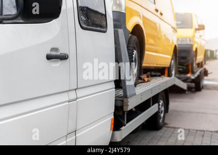 White small cargo truck car carrier loaded with two yellow van minibus on flatbed platform and semi trailer tow on roadside highway road. Volunteer Stock Photo