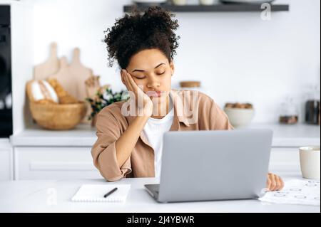Exhausted african american girl with closed eyes, freelancer or student, working remotely from home, tired of boring online work, suffering from chronic fatigue, overwork, falls asleep at the desk Stock Photo