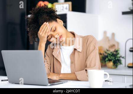 Tired overworked african american millennial pretty girl, student, freelancer, tired of remote work or study, closed her eyes, falls asleep during work, needs sleep, rest, coffee Stock Photo