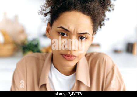 Close-up face of a frowning puzzled african american curly-haired millennial girl with freckles, knitted her eyebrows, looks unhappily at the camera, feels misunderstanding, anxiety Stock Photo