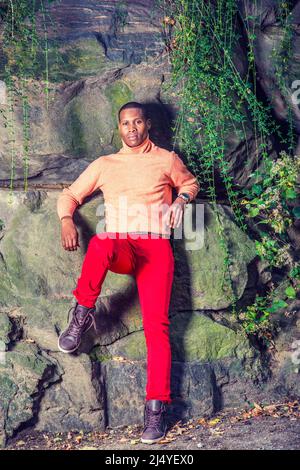 Man Autumn Casual Fashion. Dressing in light orange sweater with high collar, red pants, patterned boot shoes, wearing wristwatch, a young black guy i Stock Photo