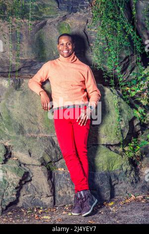 Man Autumn Casual Fashion. Dressing in light orange sweater with high collar, red pants, patterned boot shoes, wearing wristwatch, a young black guy i Stock Photo