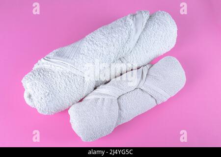 Two folded rolled white bathroom towels on pink background. Stock Photo