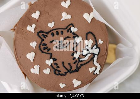 Close up of bento cake with cute picture of cat and white sugar hearts in eco box-packaging with wooden spoon. Top view. Chocolate cake Stock Photo