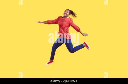 Happy African American woman in casual clothes jumping isolated on yellow background Stock Photo