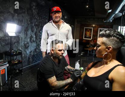 Tampa, USA. 15th Apr, 2022. Actor and former WWE star Dave Bautista watches as tattoo artist John Kural works to finish a tattoo sleeve on the arm of Mia Lanz, 41, at DC Society Ink in Tampa, Florida. Bautista and Kural are the owners of the tattoo studio, which opened in January. (Photo by Dirk Shadd/Tampa Bay Times/TNS/Sipa USA) Credit: Sipa USA/Alamy Live News Stock Photo