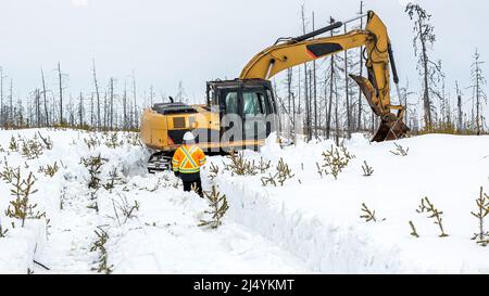 Field work with an excavator in the snow in the northern area of Canada for quarry research, horizontal Stock Photo