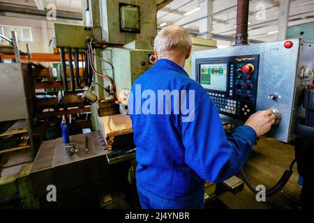 Factory engineer adjusting operation parameters of CNC lathe machine. Stock Photo