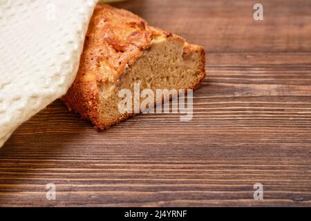 Sliced freshly baked homemade apple pie, covered with a beige napkin, towel on a brown wooden table. Homemade cakes - apple charlotte. Close-up Stock Photo