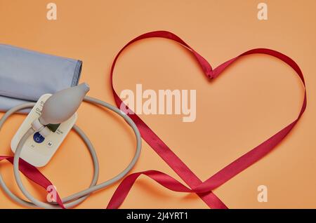 Festive background for Valentine's Day, March 8. Red satin ribbon in the shape of a heart, blood pressure monitor on a beige background. Symbol to our Stock Photo