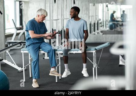Full length portrait of senior rehabilitation therapist consulting black young man in clinic Stock Photo
