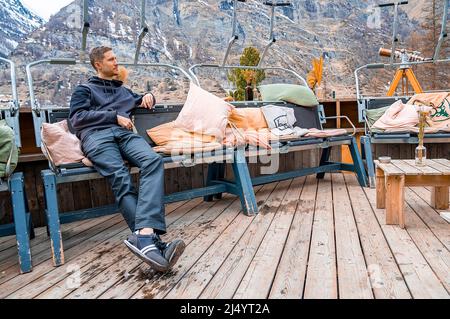 Thoughtful man resting at outdoor sitting area in resort against mountain Stock Photo