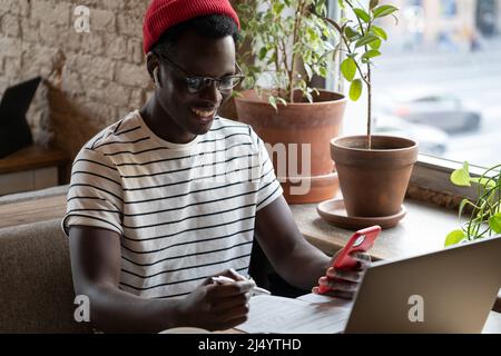 Smiling African freelancer man talking in video chat with headphones, remotely online work in cafe Stock Photo