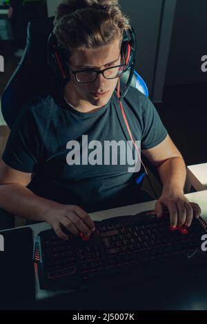 Young blond guy playing video games, playing on his laptop in the dark illuminated by the screen. Stock Photo