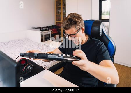 young blond man banging on the keyboard in anger at losing a video game on his computer. Young video game player. Stock Photo