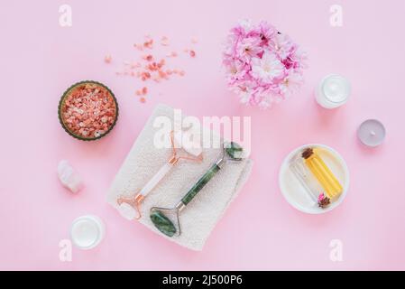 Set of natural organic spa cosmetic with sakura flowers. Flat lay bath salt, face rollers, cherry flowers, cosmetic cream and oil on pink background. Stock Photo