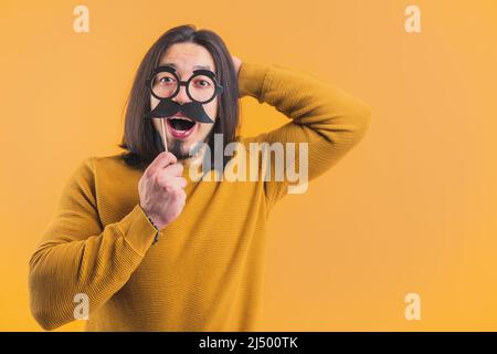 Movember - young Caucasian man holding paper glasses and moustache on the stick yellow background copy space isolated studio shot . High quality photo Stock Photo