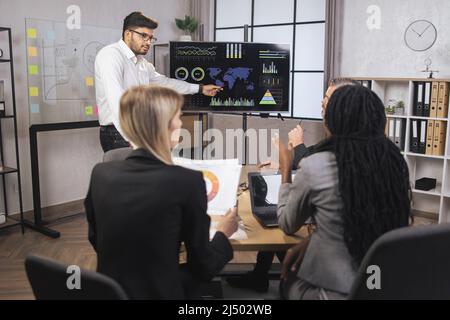 Diverse multiracial business colleagues at office boardroom, discussing business ideas together, working with papers, laptop and tablets. Brainstorming, negotiating, cooperation concept. Stock Photo