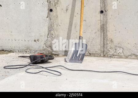 cleaning the walls from excess hardened mortar after dismantling the formwork in monolithic construction using an impact drill with a flat chisel and Stock Photo