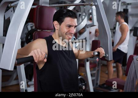 Guy training on fitness machine in gym Stock Photo