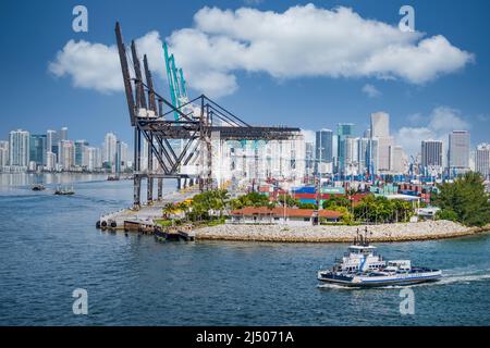 The Fisher Island Ferry sails around the Port of Miami freight container area seen from the deck of a cruise ship departing from Miami, Florida. Stock Photo