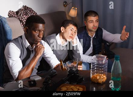 Three sad friends are watching football and cheering together Stock Photo