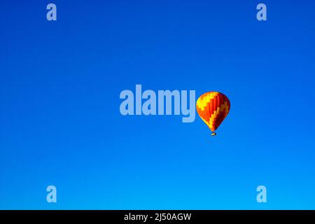 Hot Air Balloon. Single red and yellow colored hot air balloon isolated on clear blue sky background. Selective focus. Stock Photo