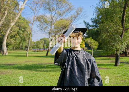 Young recent graduate boy, dressed in cap and gown, showing off his degree, celebrating on campus at the university. Very happy expression, achievemen Stock Photo