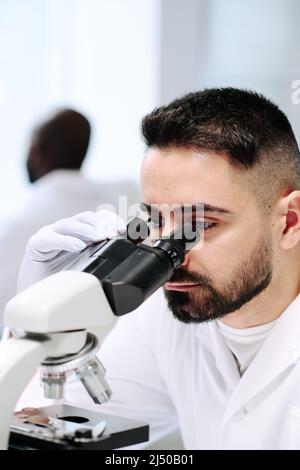 Young male worker of contemporary scientific laboratory using microscope during research of new virus or bacteria Stock Photo