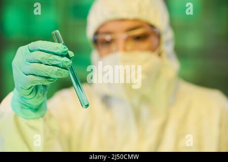 Gloved hand of contemporary virologist holding flask containing blue liquid while studying its characteristics in clinical laboratory Stock Photo