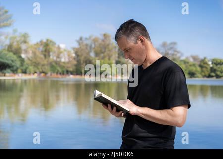 Mature man reading by a lake, enjoying free time on a sunny day Stock Photo