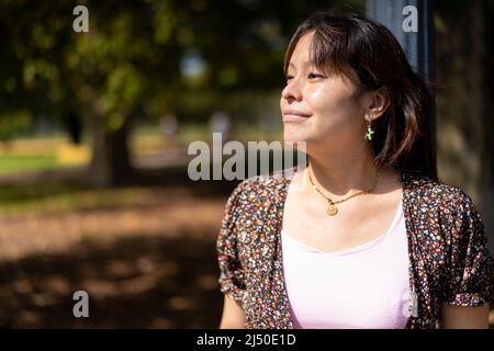 Portrait of a young Latin woman in a park leaning on a lamppost, enjoying the sun's rays on her skin Stock Photo