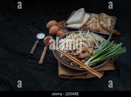 Stir fried soft turnip cake or Fried radish cake (chai tow kway) with bean sprout and chives in ceramic plate served with suger, ground dried chili. T Stock Photo