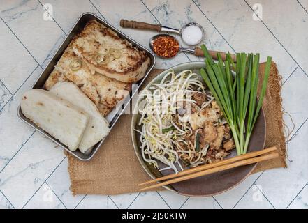 Stir fried soft turnip cake or Fried radish cake (chai tow kway) with bean sprout and chives in ceramic plate served with suger, ground dried chili. T Stock Photo