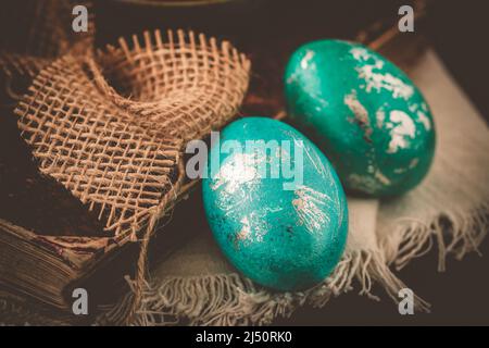 Two green and turquoise metallic Easter eggs with an antique book on a dark brown vintage background Stock Photo