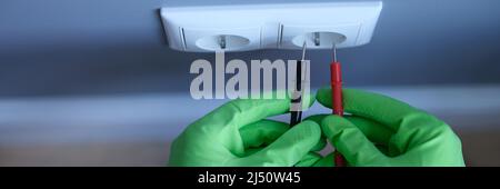 Craftsman in rubber gloves holding tester near electrical outlet at home closeup Stock Photo
