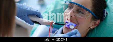 Young woman dentist in protective gloves checking dental seal, fixing photopolymer lamp during stomatology procedure Stock Photo