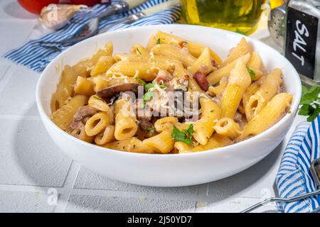 Italian mediterranean lunch concept. Penne pasta with creamy carbonara mushroom sauce. On a white tile table, with spices for dinner copy space Stock Photo