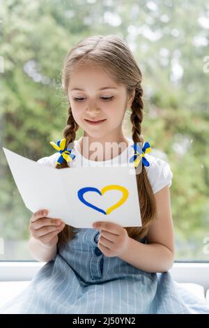 positive patriotic girl reading postcard with blue and yellow heart Stock Photo